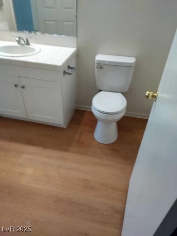 half bathroom with baseboards, vanity, toilet, and wood finished floors