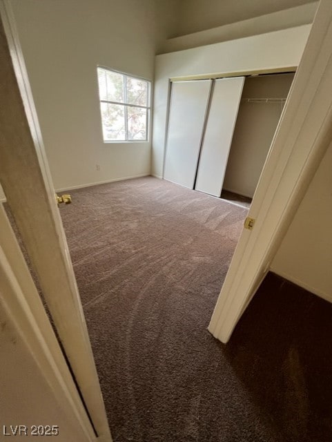 unfurnished bedroom featuring dark colored carpet, a closet, and baseboards