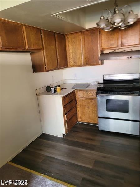 kitchen featuring dark wood-style flooring, light countertops, brown cabinets, stainless steel electric range oven, and an inviting chandelier