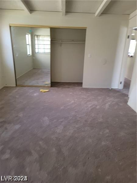 unfurnished bedroom with beamed ceiling and a closet