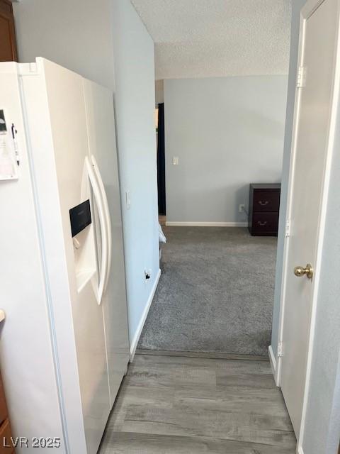 hallway with a textured ceiling, carpet, wood finished floors, and baseboards