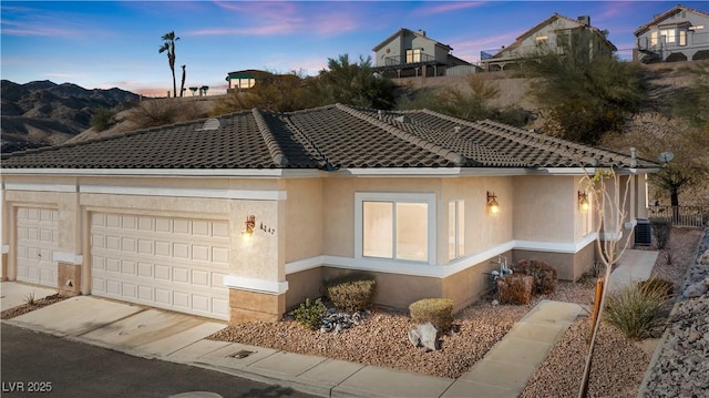 view of front of house featuring driveway, a garage, a tiled roof, central air condition unit, and stucco siding