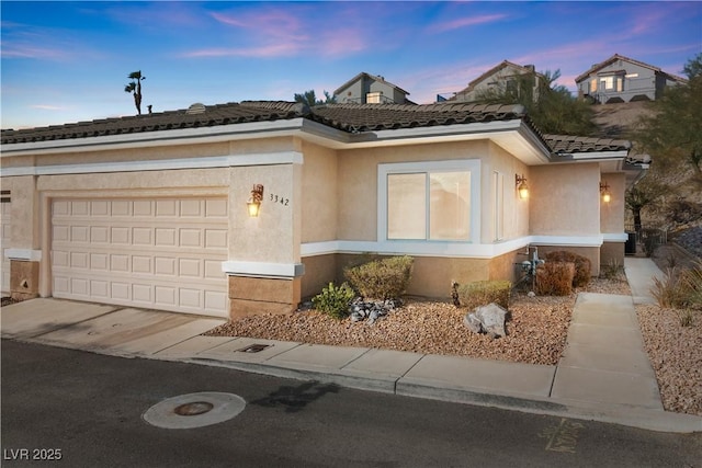 view of front of property featuring driveway, an attached garage, a tiled roof, and stucco siding