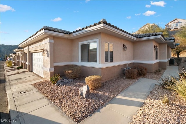 view of property exterior featuring concrete driveway, a tiled roof, an attached garage, and stucco siding