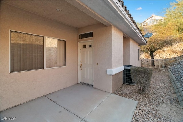 doorway to property with central AC, a patio, fence, and stucco siding