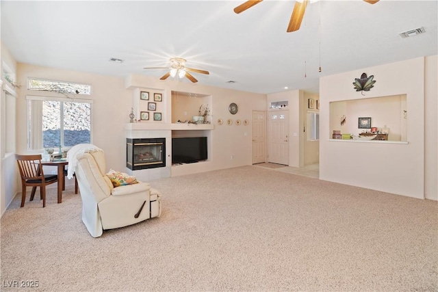 living area featuring a ceiling fan, visible vents, light carpet, and a tiled fireplace