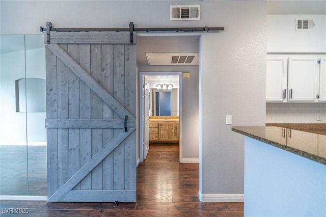 hallway featuring a barn door, visible vents, and dark wood-type flooring