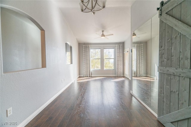 spare room featuring ceiling fan with notable chandelier, a barn door, wood finished floors, and baseboards