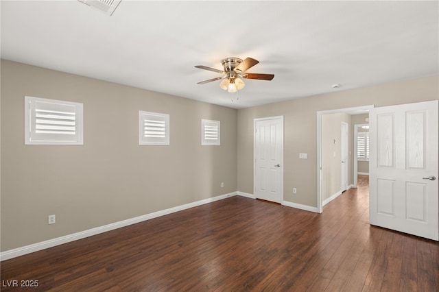 empty room with dark wood-style floors, a ceiling fan, visible vents, and baseboards