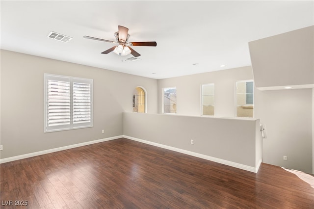 empty room featuring dark wood-style flooring, visible vents, ceiling fan, and baseboards