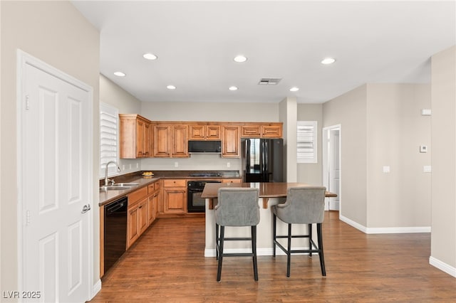 kitchen with visible vents, dark wood finished floors, a breakfast bar area, a center island, and black appliances