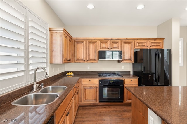 kitchen with recessed lighting, a sink, dark wood-style floors, black appliances, and dark stone countertops