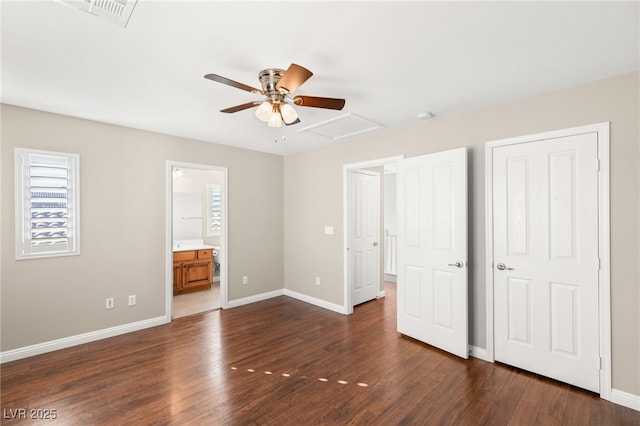 unfurnished bedroom with ensuite bath, attic access, baseboards, and dark wood-style flooring