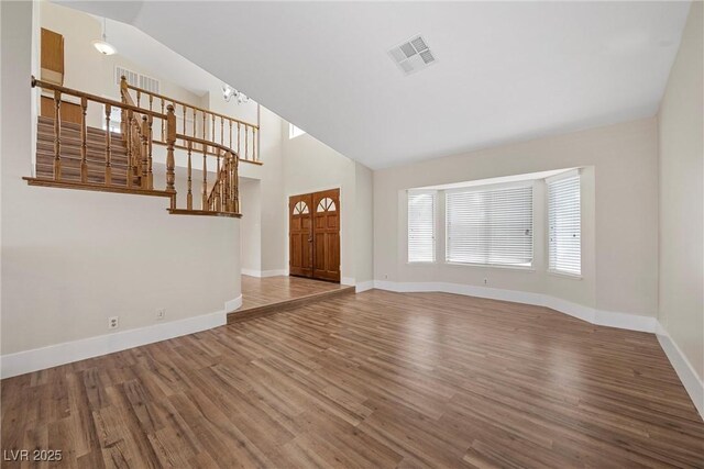 interior space featuring baseboards, visible vents, stairway, wood finished floors, and high vaulted ceiling