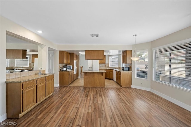 kitchen featuring white appliances, a sink, visible vents, brown cabinets, and decorative backsplash