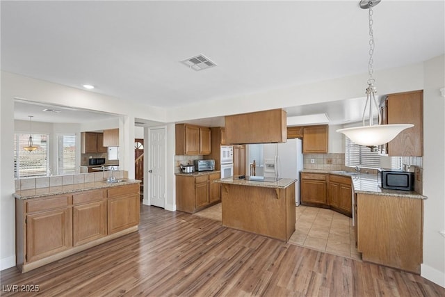 kitchen with a center island, light wood finished floors, decorative backsplash, brown cabinetry, and black microwave