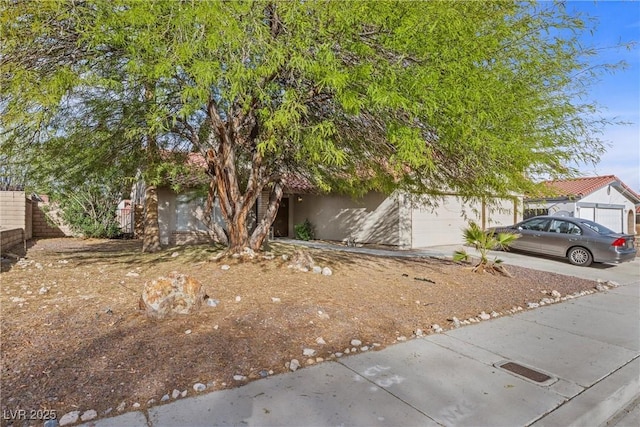 obstructed view of property featuring a garage, driveway, fence, and stucco siding