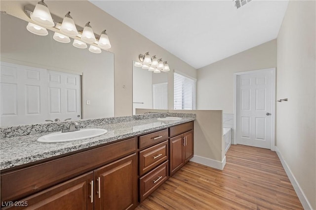 bathroom with lofted ceiling, double vanity, a sink, and wood finished floors