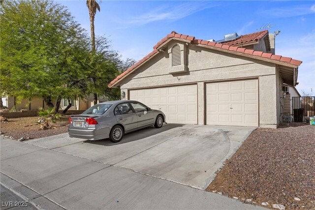 view of side of home with a garage, concrete driveway, a tiled roof, and stucco siding