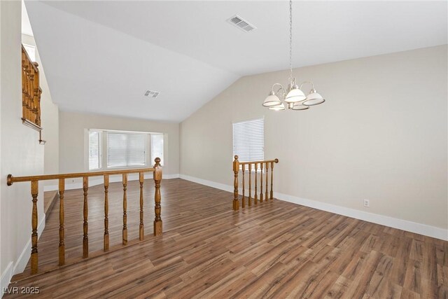 empty room with wood finished floors, visible vents, baseboards, vaulted ceiling, and an inviting chandelier