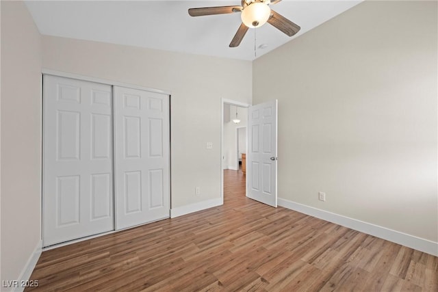 unfurnished bedroom featuring wood finished floors, a ceiling fan, baseboards, vaulted ceiling, and a closet