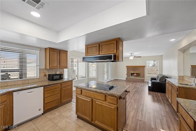 kitchen featuring visible vents, under cabinet range hood, black appliances, a fireplace, and a sink