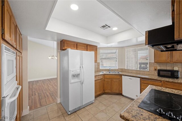 kitchen featuring visible vents, brown cabinets, a tray ceiling, black appliances, and a sink