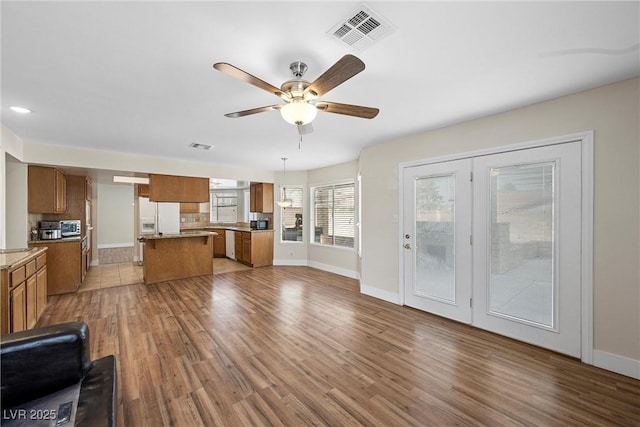 unfurnished living room featuring a ceiling fan, visible vents, baseboards, and wood finished floors