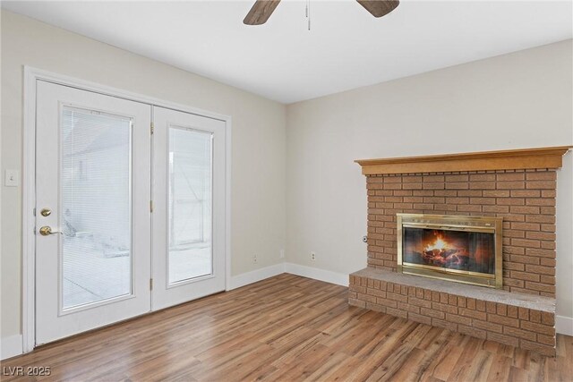 unfurnished living room with a brick fireplace, ceiling fan, baseboards, and wood finished floors