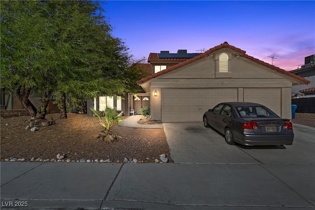 view of front of home with a tile roof, stucco siding, roof mounted solar panels, a garage, and driveway