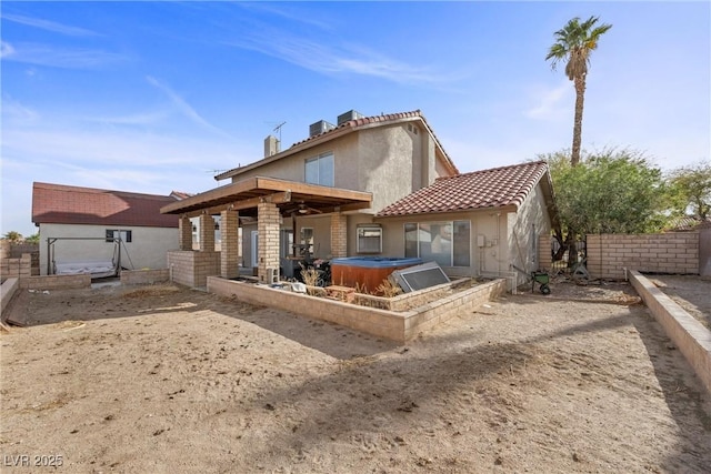 back of property with a tiled roof, fence, a hot tub, and stucco siding