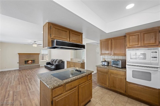 kitchen with a toaster, a fireplace, decorative backsplash, white appliances, and under cabinet range hood