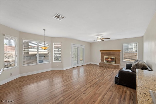 unfurnished living room featuring ceiling fan, visible vents, baseboards, light wood-type flooring, and a brick fireplace