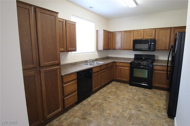 kitchen featuring dark countertops, brown cabinets, stone finish flooring, black appliances, and a sink