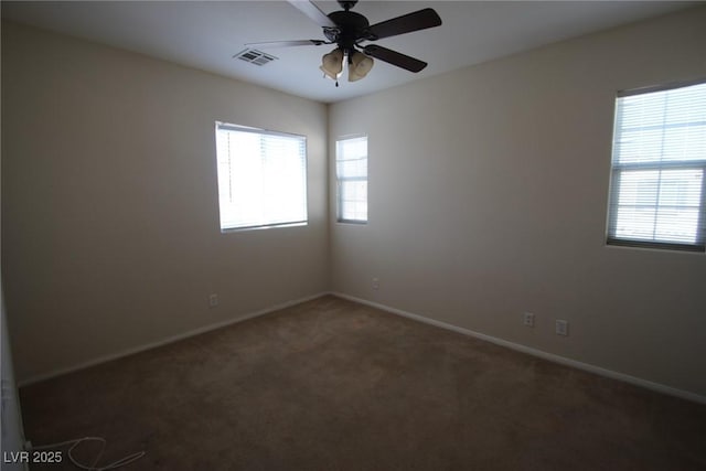 unfurnished room with ceiling fan, dark carpet, visible vents, and baseboards