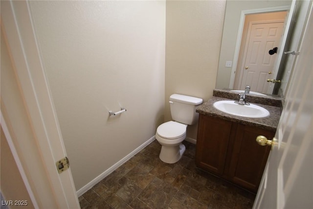 half bathroom featuring stone finish floor, vanity, toilet, and baseboards