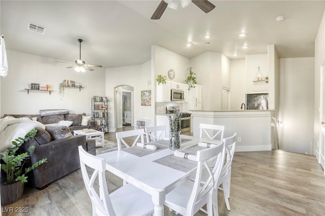 dining room featuring arched walkways, ceiling fan, visible vents, and light wood-style flooring