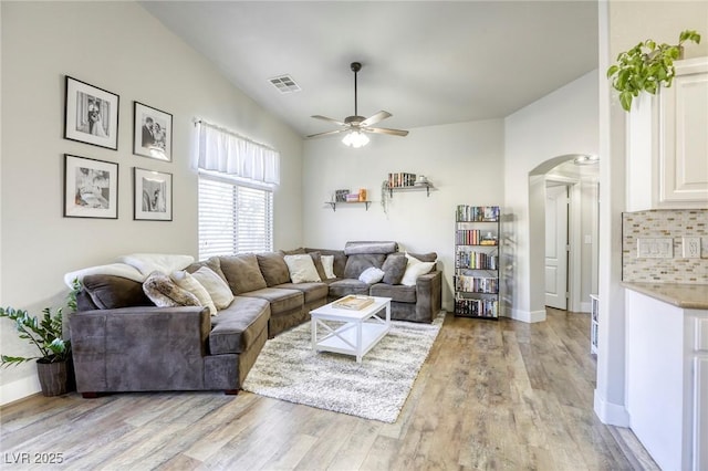 living area featuring arched walkways, visible vents, a ceiling fan, vaulted ceiling, and light wood-type flooring