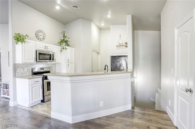 kitchen with stainless steel appliances, a peninsula, white cabinetry, light countertops, and tasteful backsplash