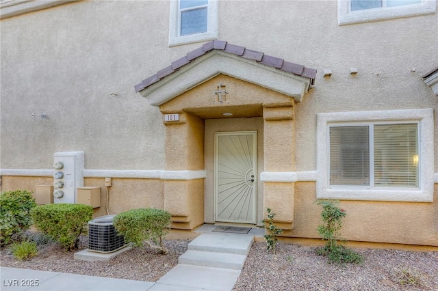 view of exterior entry featuring cooling unit and stucco siding