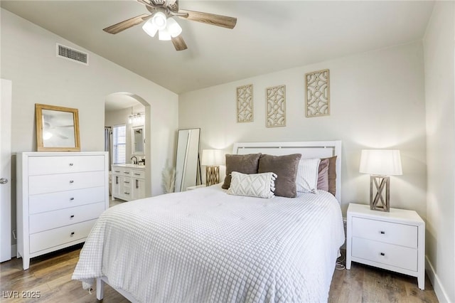 bedroom with arched walkways, visible vents, vaulted ceiling, and wood finished floors