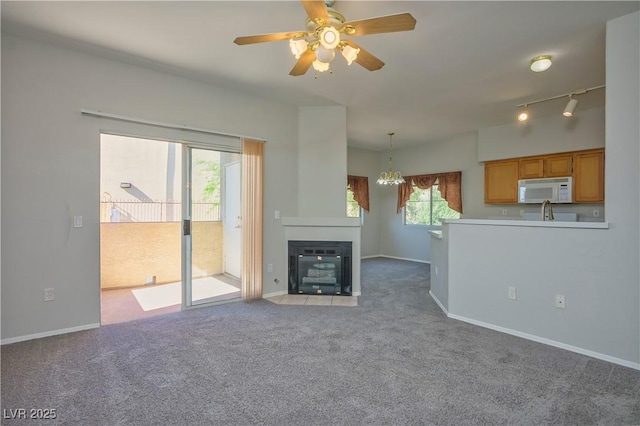 unfurnished living room featuring rail lighting, a fireplace with flush hearth, light carpet, baseboards, and ceiling fan with notable chandelier