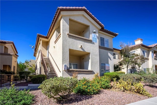 back of property featuring a tile roof, stairway, and stucco siding