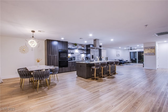 kitchen featuring a kitchen island with sink, light wood-style flooring, island exhaust hood, and visible vents