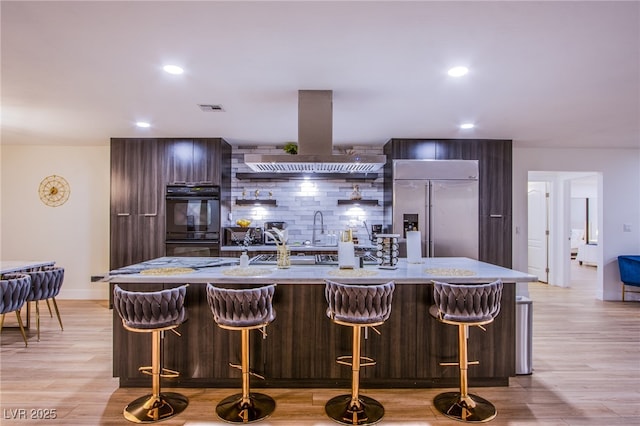 kitchen featuring visible vents, island exhaust hood, built in fridge, dobule oven black, and modern cabinets