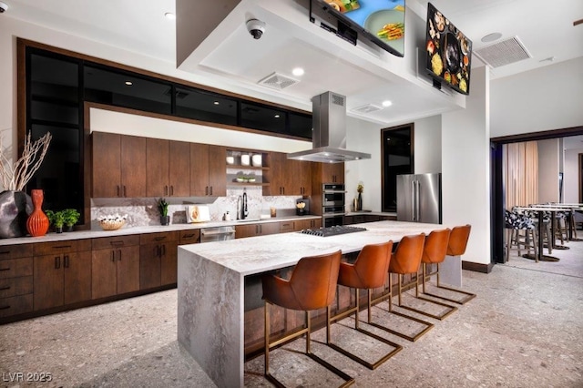 kitchen with a breakfast bar, island exhaust hood, light countertops, decorative backsplash, and appliances with stainless steel finishes