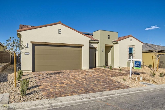 mediterranean / spanish house featuring decorative driveway, an attached garage, a tile roof, and stucco siding