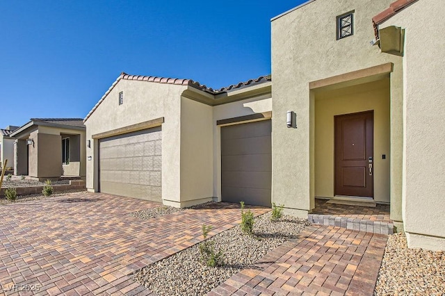 view of exterior entry with decorative driveway, a tile roof, and stucco siding