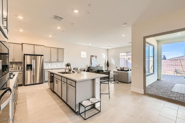 kitchen featuring light countertops, appliances with stainless steel finishes, a center island with sink, and gray cabinetry