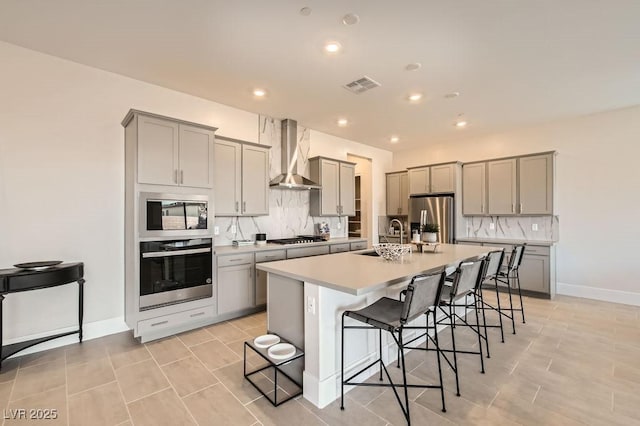 kitchen with a center island with sink, visible vents, wall chimney exhaust hood, a breakfast bar area, and stainless steel appliances